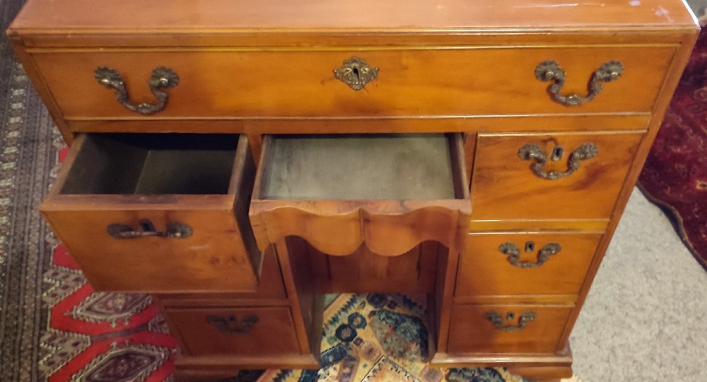 A rectangular yew wood kneehole desk featuring multiple drawers, a central recessed cupboard door, and brass drop handles. View III