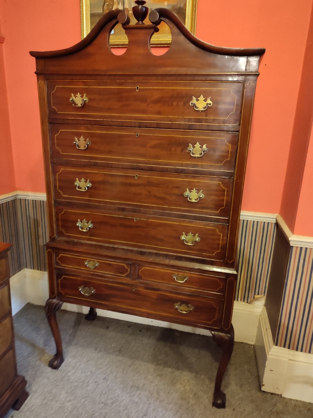 A tall 19th-century mahogany chest on stand featuring a swan-neck pediment with finial, line-inlaid drawer fronts, brass swan-neck handles, and cabriole legs.