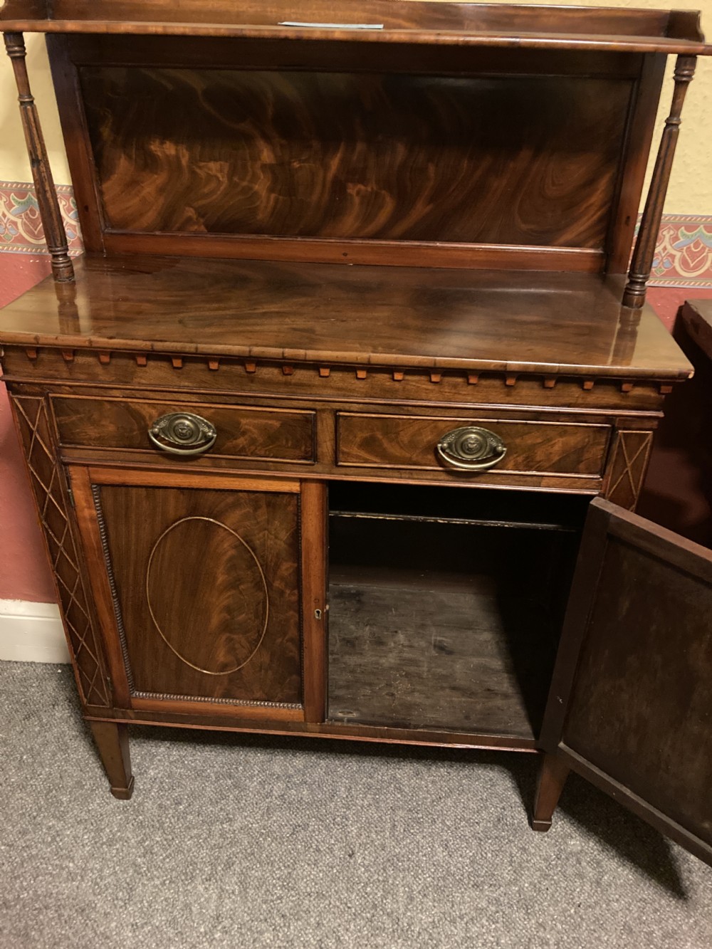 A Regency mahogany side cabinet featuring an upper gallery shelf on turned supports, two drawers, oval-inlaid cupboard doors, and tapered square legs. View III