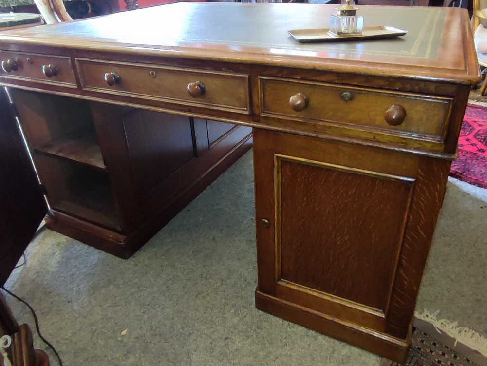 A nineteenth-century oak partners desk featuring a leather inset top, turned wooden knobs, and twin pedestal bases with drawers.
