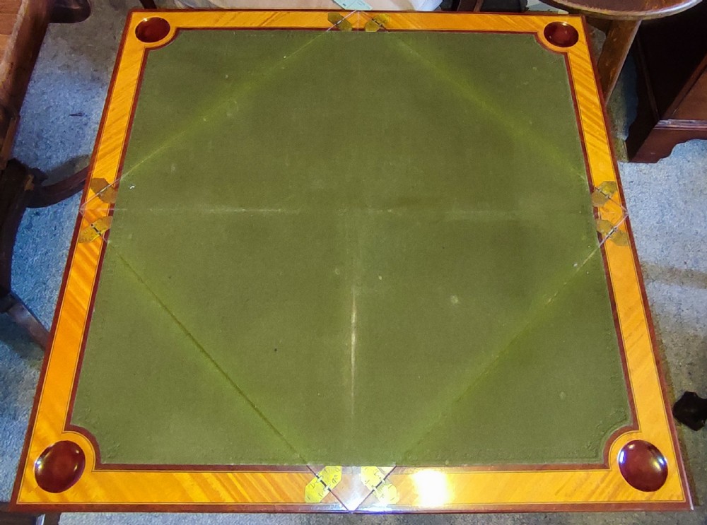 An Edwardian satinwood envelope card table featuring detailed marquetry inlays, four triangular top flaps, a single frieze drawer, and square tapered legs with a lower undertier. View IV