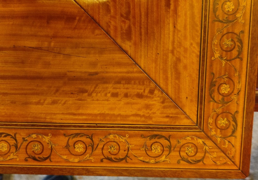 An Edwardian satinwood envelope card table featuring detailed marquetry inlays, four triangular top flaps, a single frieze drawer, and square tapered legs with a lower undertier. View VI