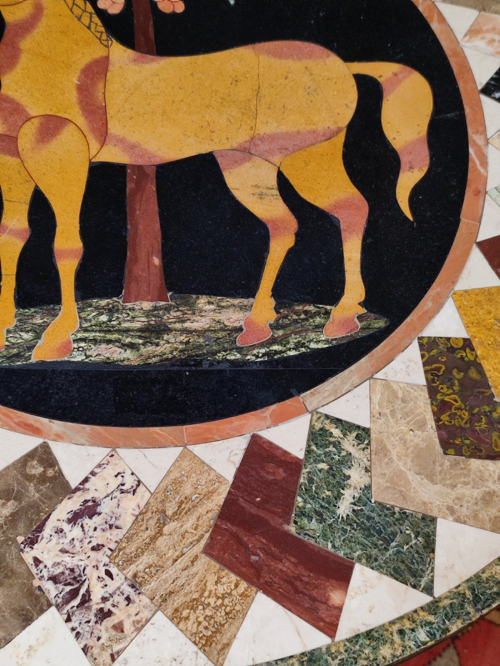 A circular specimen marble tabletop decorated with a central inlaid horse motif and geometric border, supported by a painted cream cast iron tripod base. View III