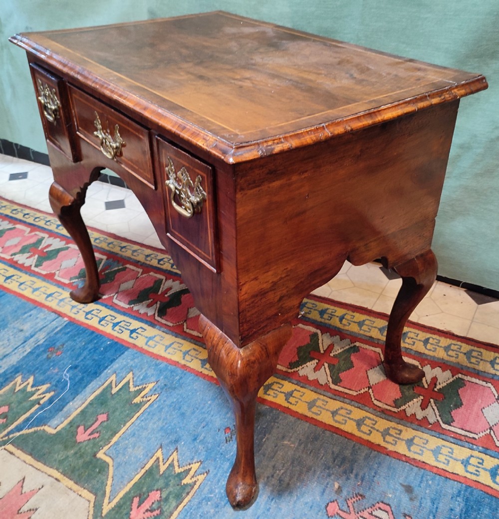 An 18th-century George III walnut lowboy table featuring three inlaid drawers, brass handles, a shaped apron, and four cabriole legs.