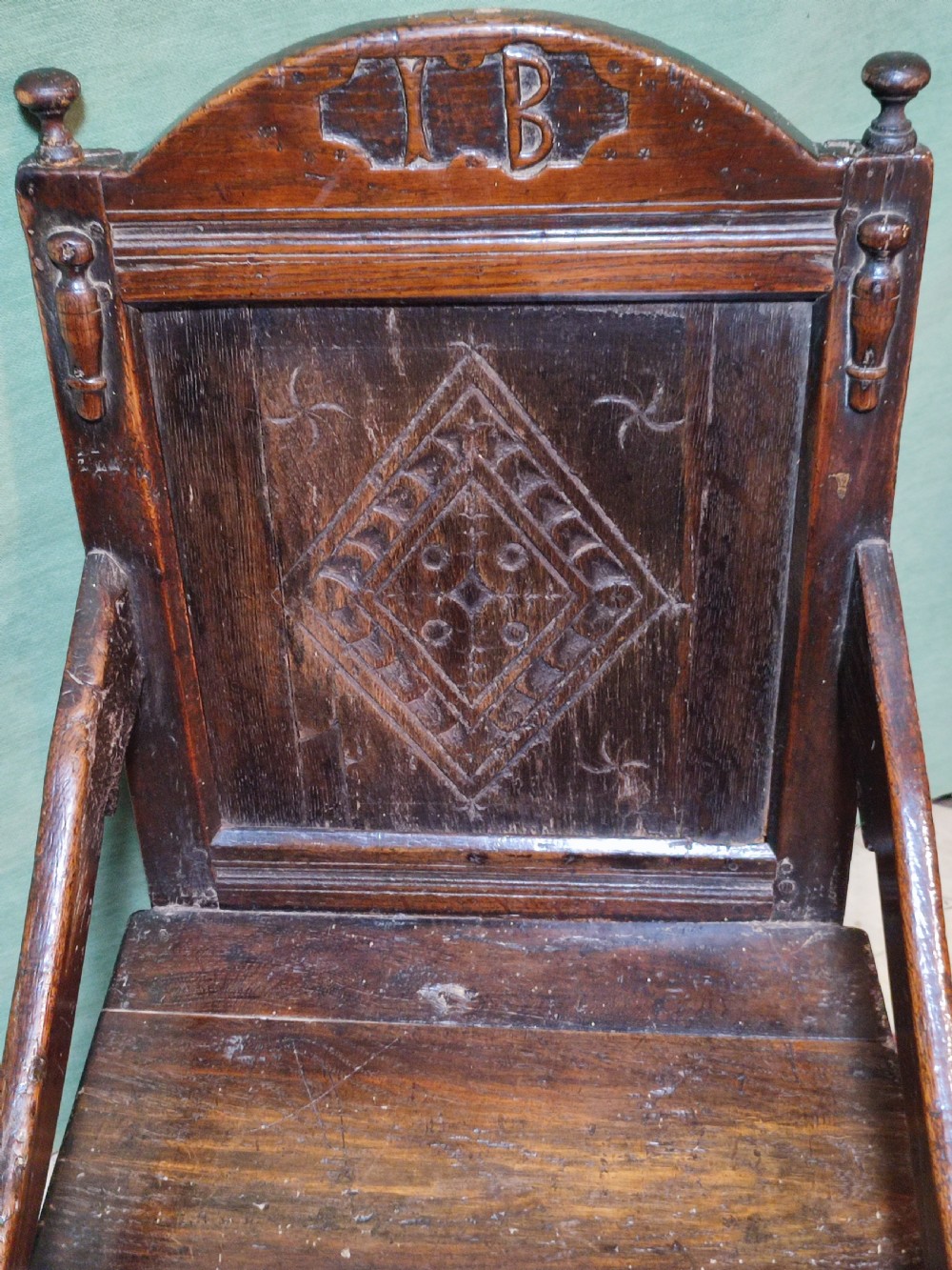 A 17th-century carved dark oak wainscot armchair featuring a carved lozenge back panel, carved initials on the crest rail, and turned front legs. View III