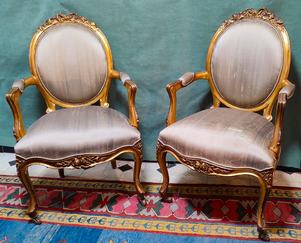 A pair of 19th-century French style giltwood fauteuil armchairs with oval medallion backs and light grey silk upholstery.