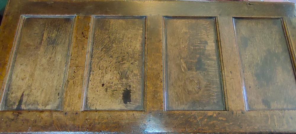 A seventeenth-century warm brown solid oak coffer featuring a four-panel lid, panelled front, and central iron lock plate. View IV