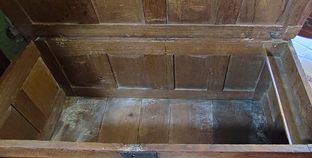 A seventeenth-century warm brown solid oak coffer featuring a four-panel lid, panelled front, and central iron lock plate. View V