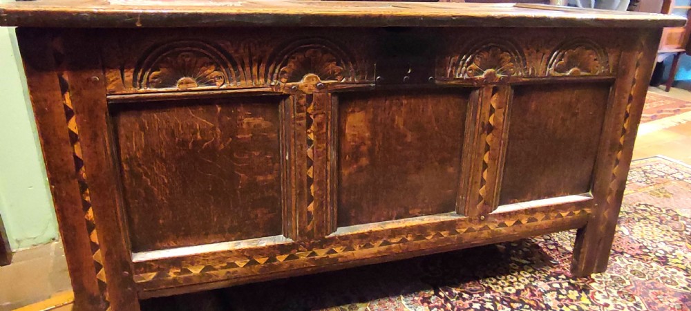 A 17th century dark oak coffer featuring carved lunette arches, inlaid geometric borders, three front panels, and a fitted iron lock escutcheon. View V