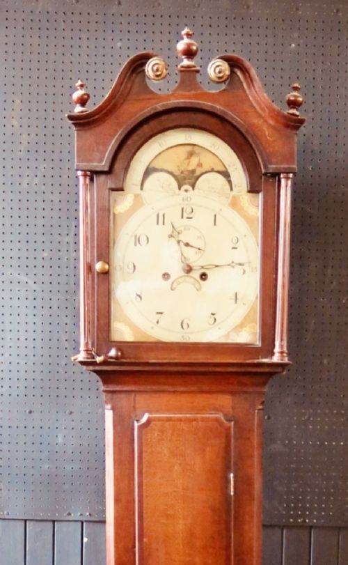fig 1. A Georgian mahogany longcase clock with a swan-neck pediment, brass finials, painted arch dial, and a tall timber trunk casing.