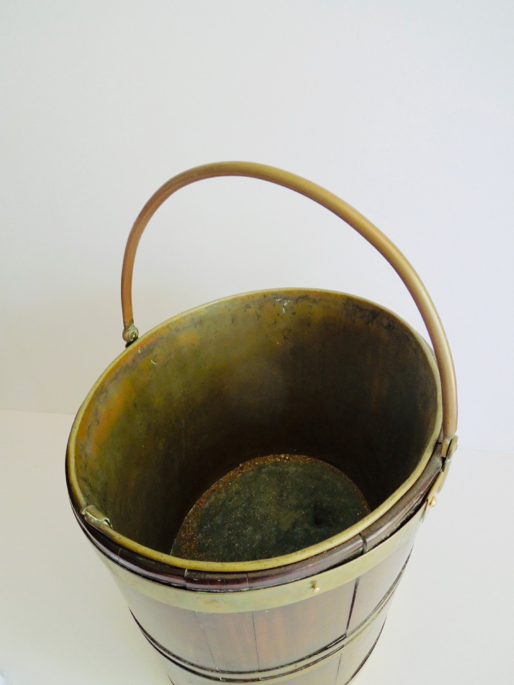 An oval mahogany wine bucket constructed from timber staves, bound by three polished brass hoops, and fitted with an arched brass swing handle. View IV