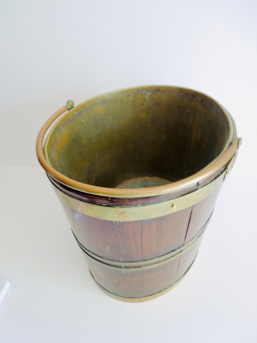 An oval mahogany wine bucket constructed from timber staves, bound by three polished brass hoops, and fitted with an arched brass swing handle. View V