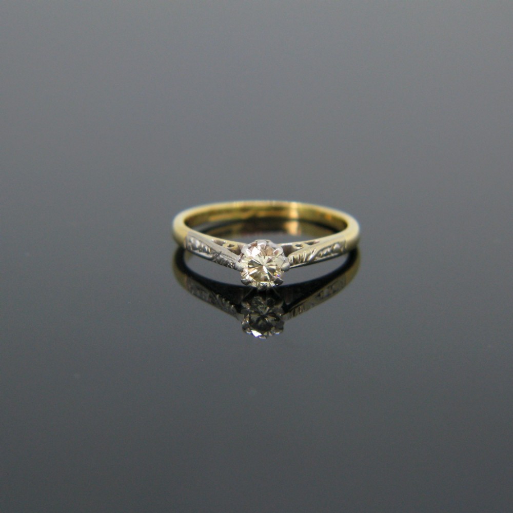 An 18kt yellow gold and platinum solitaire ring set with a central diamond in a carved mount.