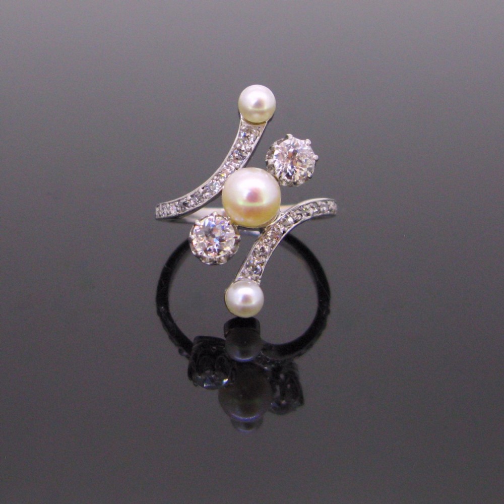 An Edwardian platinum and white gold crossover ring set with central natural pearls and round diamonds along curved shoulders.