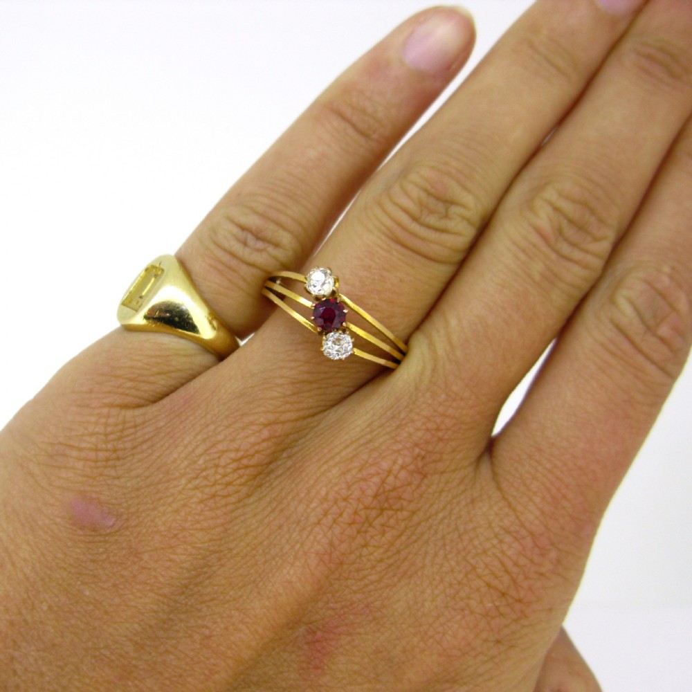 An antique yellow gold Victorian ring featuring a triple wire shank set with a central red ruby flanked by two bright diamonds. View VI