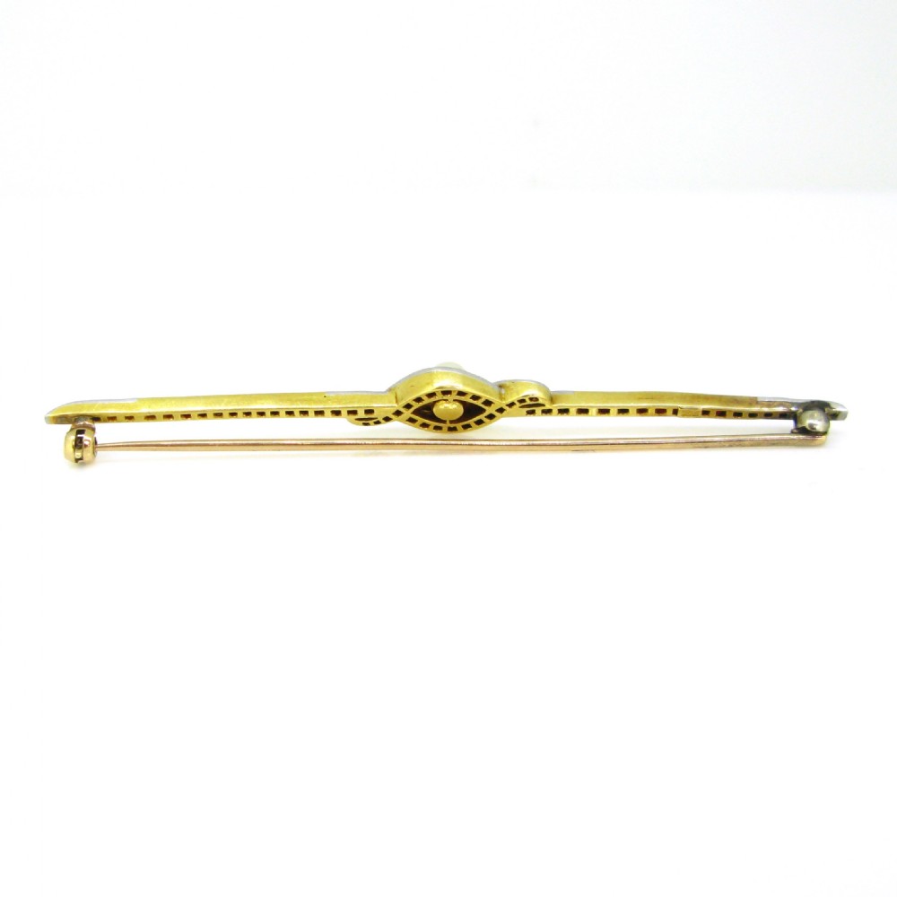 An Edwardian platinum and gold bar brooch set with calibre-cut red rubies, diamonds, and a central pearl. View IV