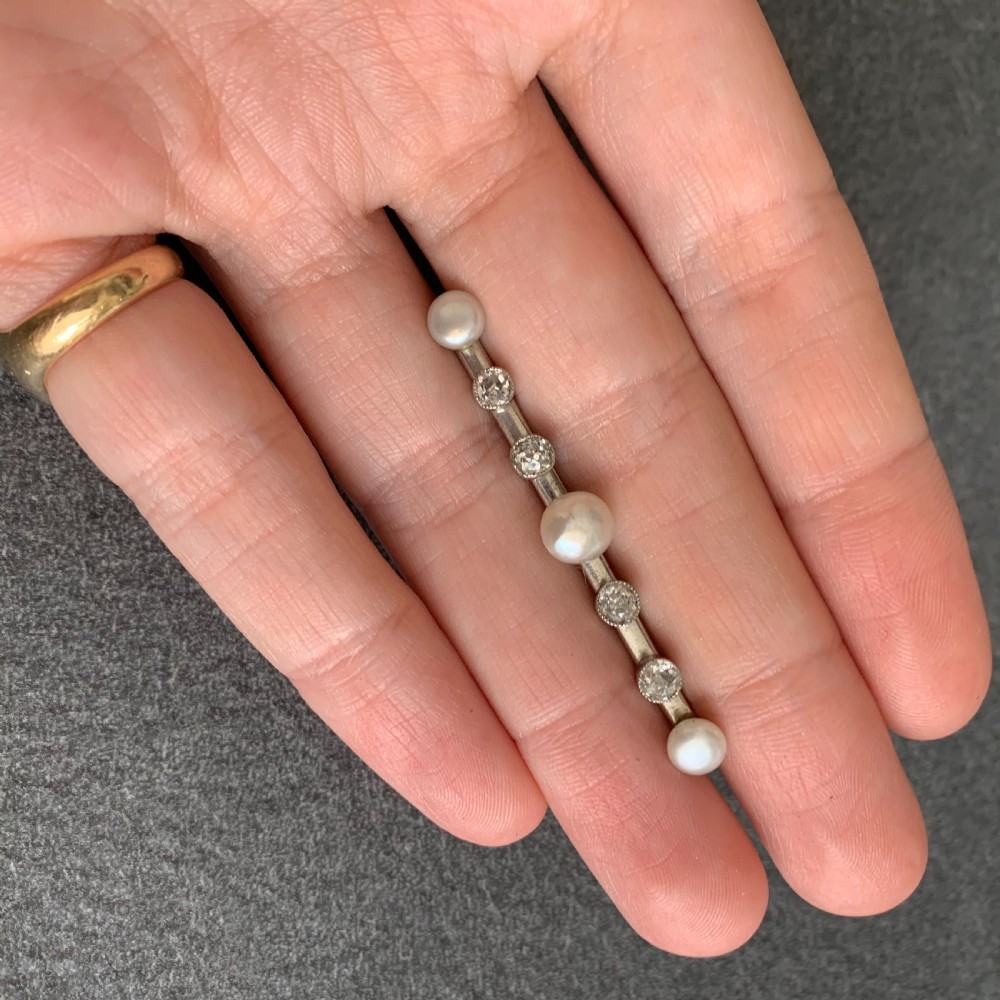 An Edwardian platinum and white gold bar brooch featuring a linear arrangement of natural pearls and round old-cut diamonds. View IX