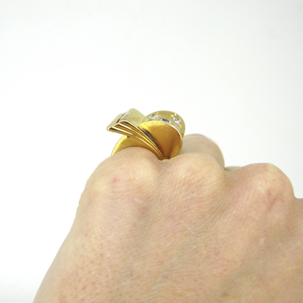 An 18ct yellow gold 1940s Retro Tank ring featuring a sculptural scroll motif set with diamonds and channel-set red rubies. View VI