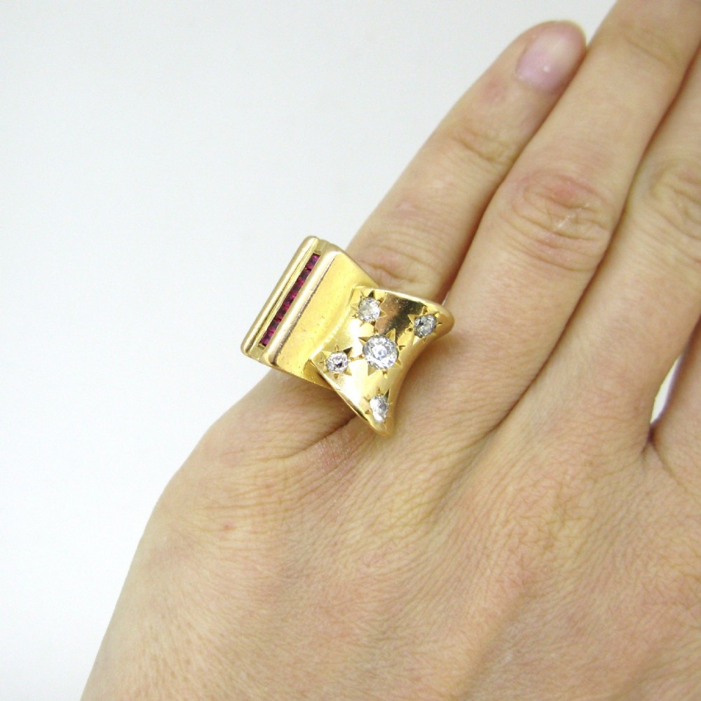 An 18ct yellow gold 1940s Retro Tank ring featuring a sculptural scroll motif set with diamonds and channel-set red rubies. View VII