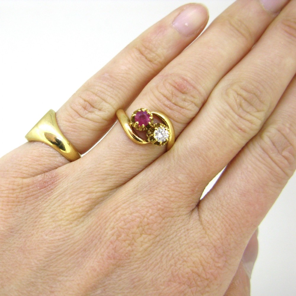 An 18kt yellow gold crossover ring set with a faceted ruby and a diamond in claw settings. View VII