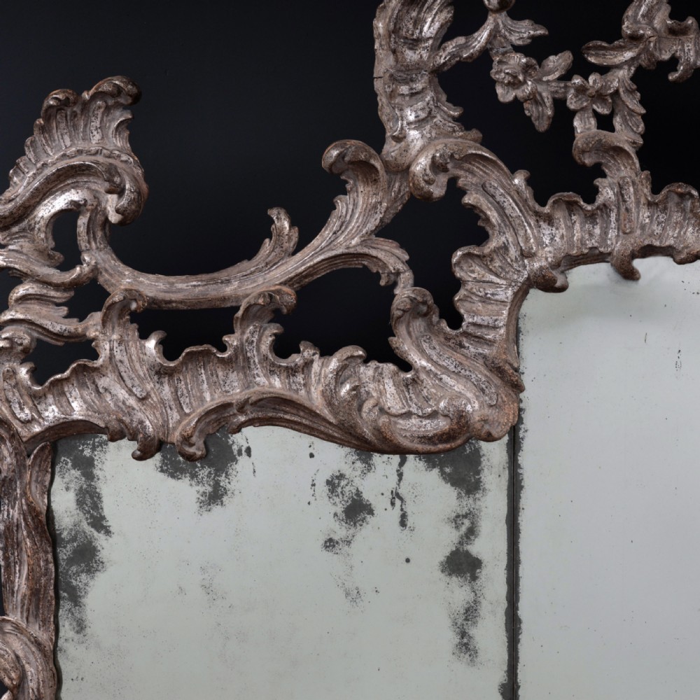 An 18th-century silvered Rococo overmantel mirror featuring an elaborately carved crest with C-scrolls and a tripartite mirror plate with visible foxing. View III