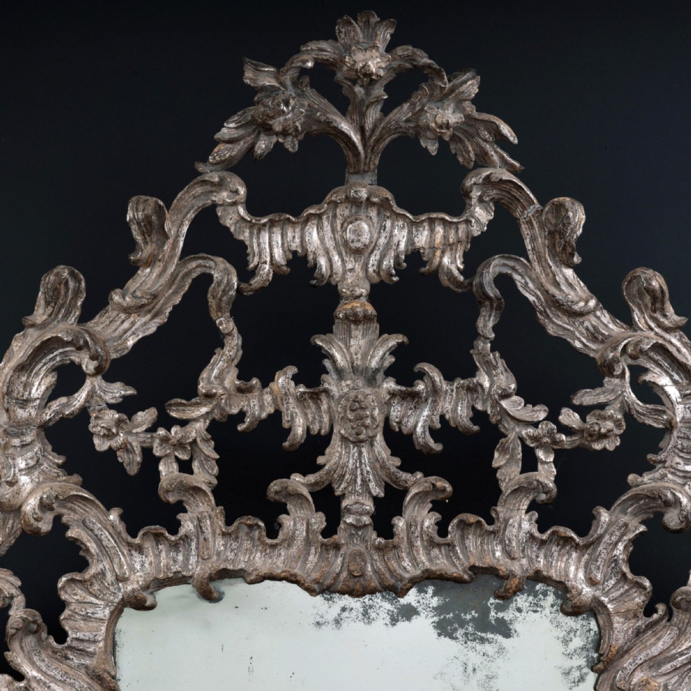 An 18th-century silvered Rococo overmantel mirror featuring an elaborately carved crest with C-scrolls and a tripartite mirror plate with visible foxing. View IV