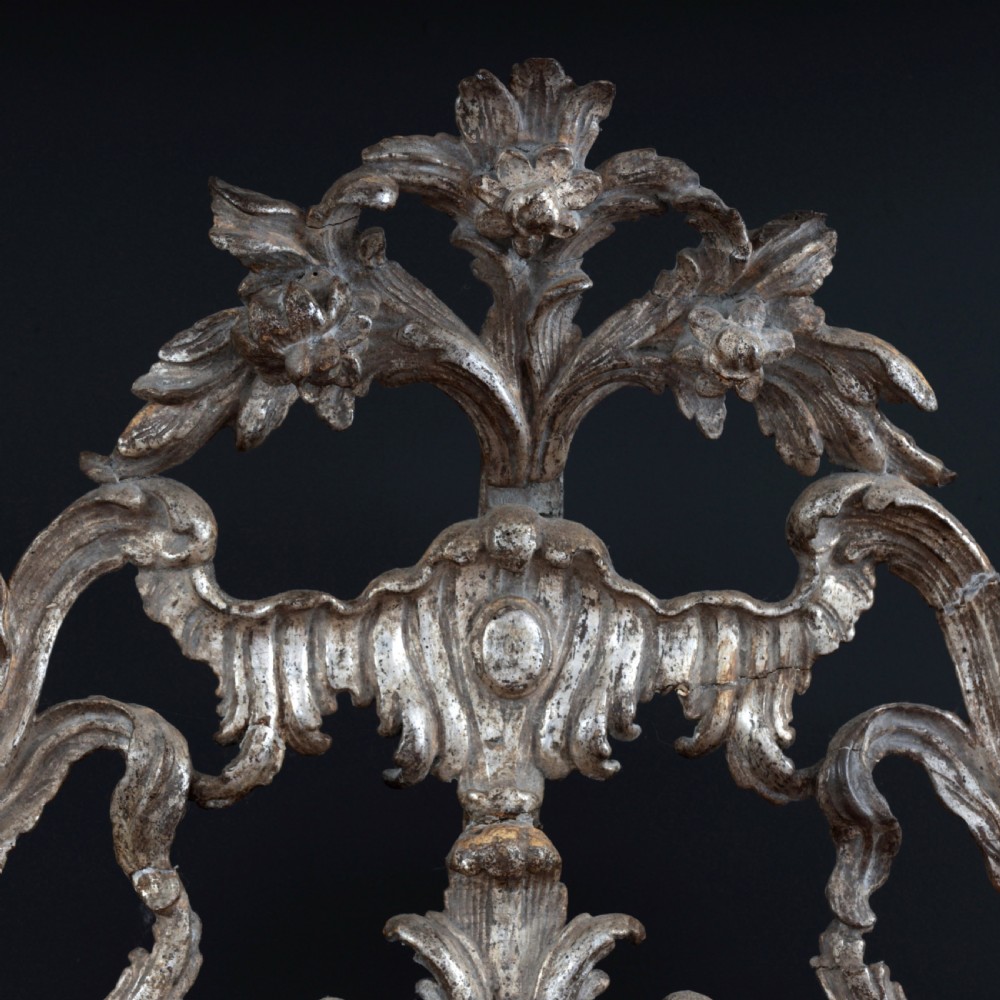 An 18th-century silvered Rococo overmantel mirror featuring an elaborately carved crest with C-scrolls and a tripartite mirror plate with visible foxing. View XI