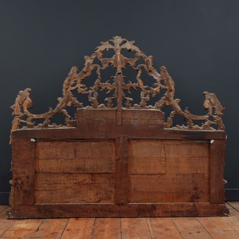 An 18th-century silvered Rococo overmantel mirror featuring an elaborately carved crest with C-scrolls and a tripartite mirror plate with visible foxing. View XVII
