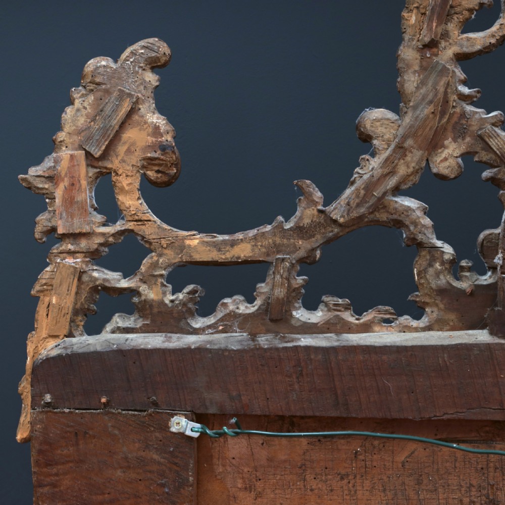 An 18th-century silvered Rococo overmantel mirror featuring an elaborately carved crest with C-scrolls and a tripartite mirror plate with visible foxing. View XX