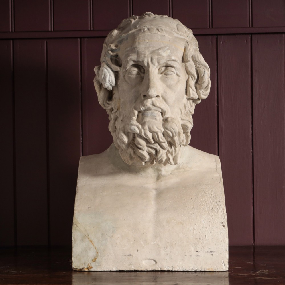 An off-white plaster bust depicting the classical Greek poet Homer with a detailed curly beard and headband, set on a flat square base.