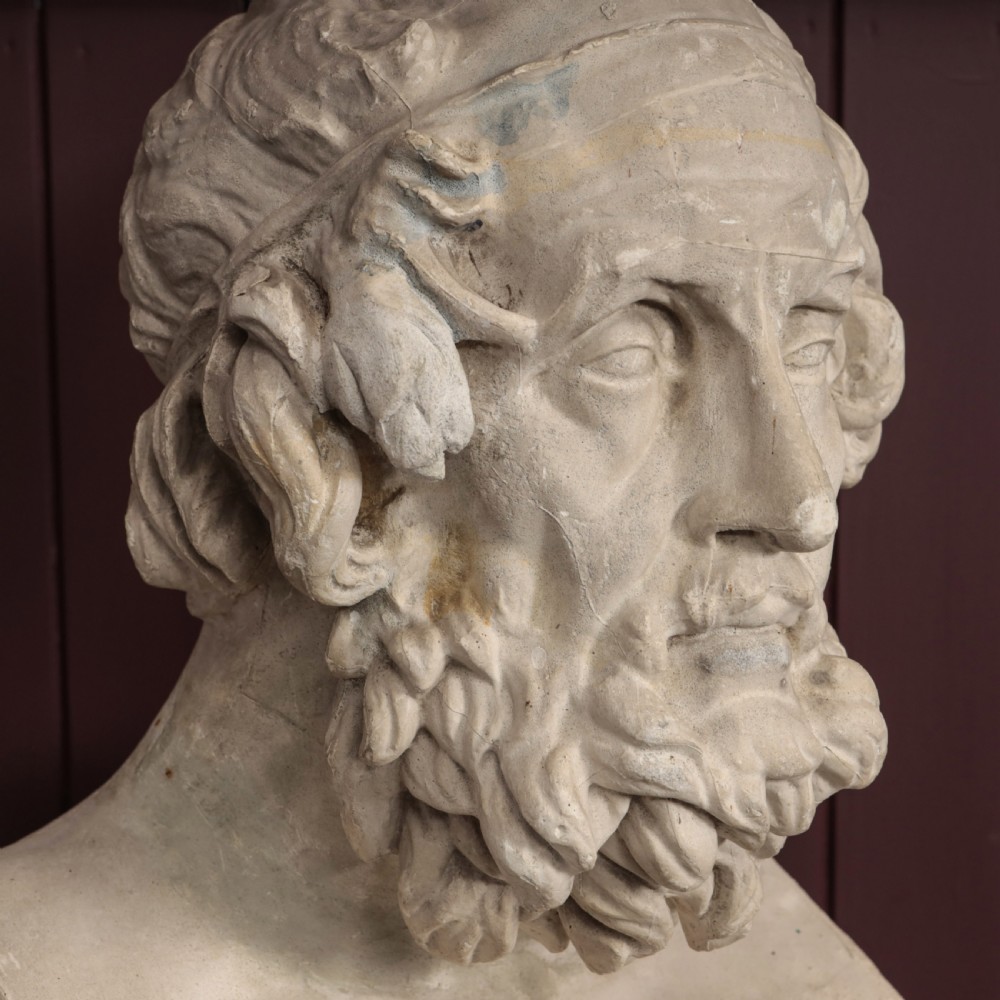 An off-white plaster bust depicting the classical Greek poet Homer with a detailed curly beard and headband, set on a flat square base. View II