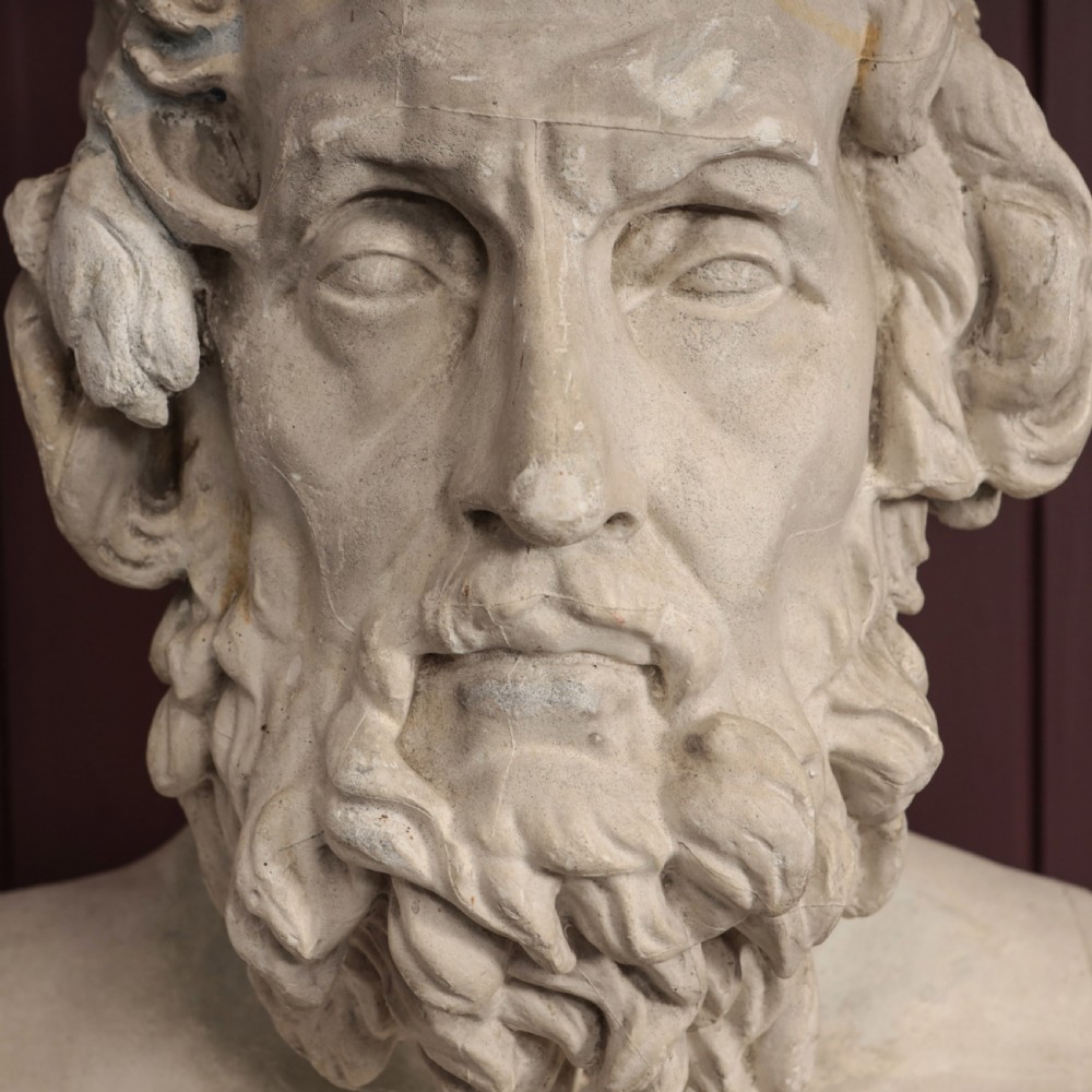 An off-white plaster bust depicting the classical Greek poet Homer with a detailed curly beard and headband, set on a flat square base. View III