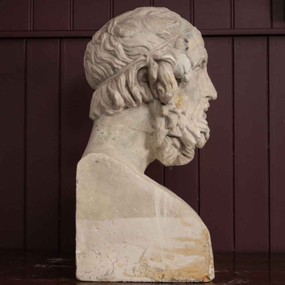 An off-white plaster bust depicting the classical Greek poet Homer with a detailed curly beard and headband, set on a flat square base. View VI