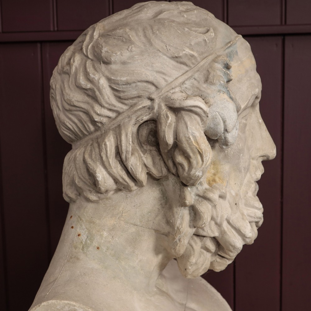 An off-white plaster bust depicting the classical Greek poet Homer with a detailed curly beard and headband, set on a flat square base. View VII