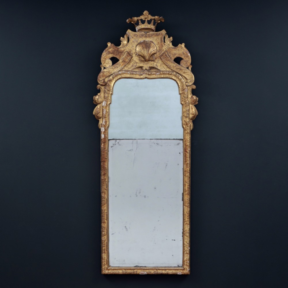 A tall George I period giltwood wall mirror featuring an ornate carved crown cresting, shell motif, and a two-section mirror plate.