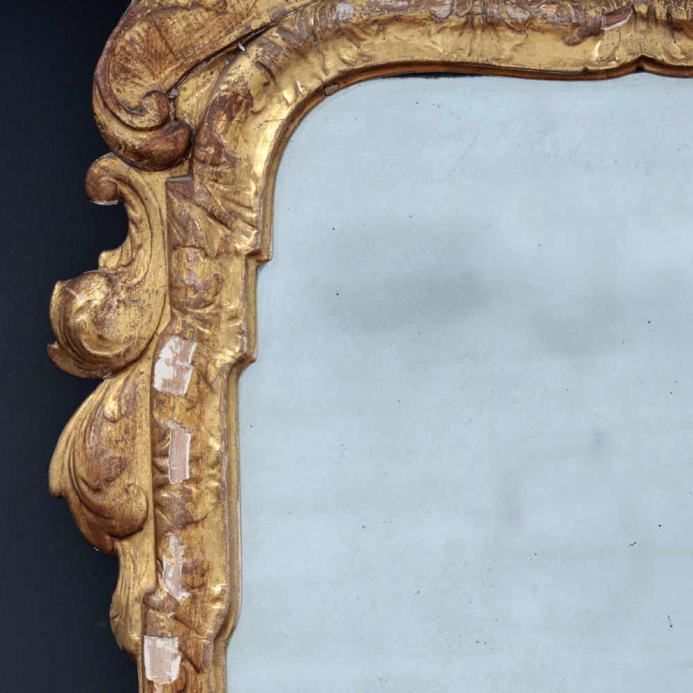 A tall George I period giltwood wall mirror featuring an ornate carved crown cresting, shell motif, and a two-section mirror plate. View II