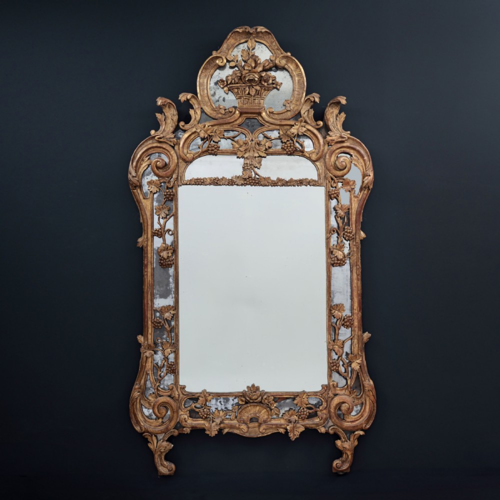 An ornate Louis XV style gilded mirror featuring a carved timber frame with vine motifs and a flower basket crest.