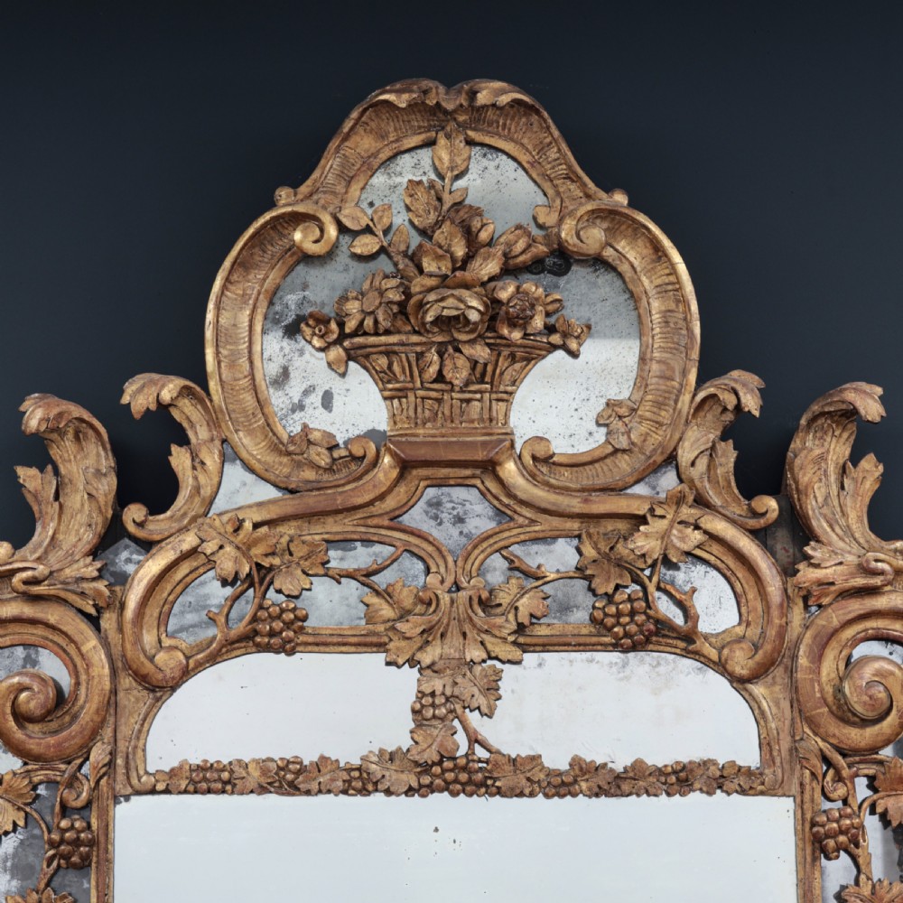 An ornate Louis XV style gilded mirror featuring a carved timber frame with vine motifs and a flower basket crest. View II