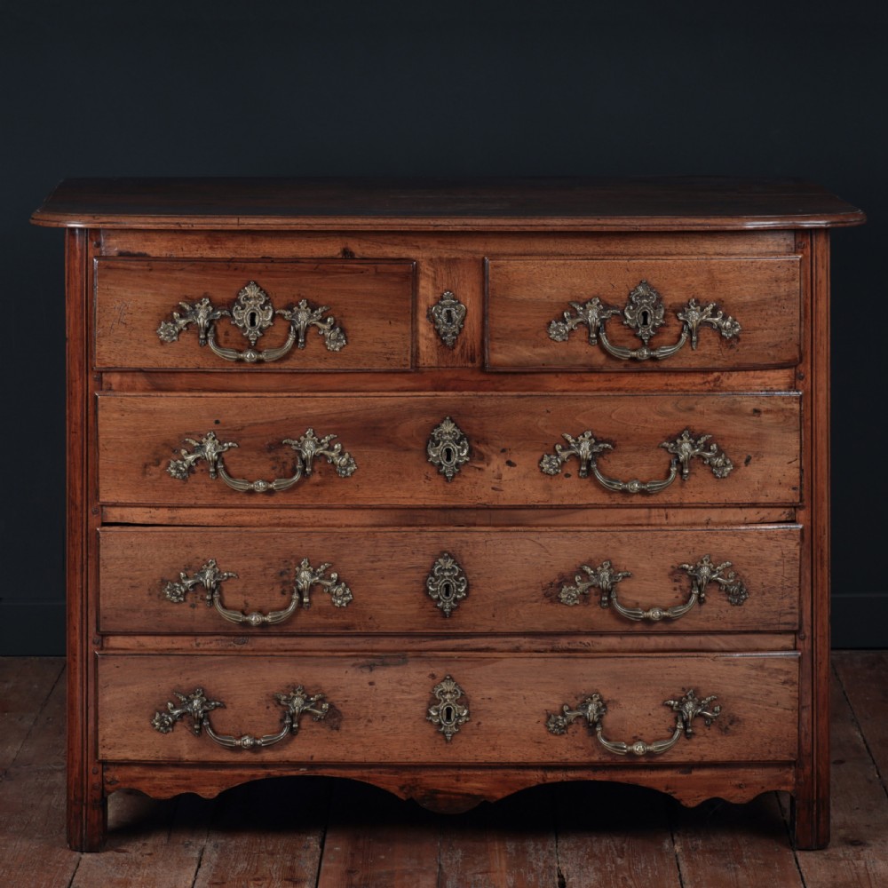 A French Louis XV style warm walnut commode featuring four drawer levels with ornate brass scroll handles and keyhole escutcheons.