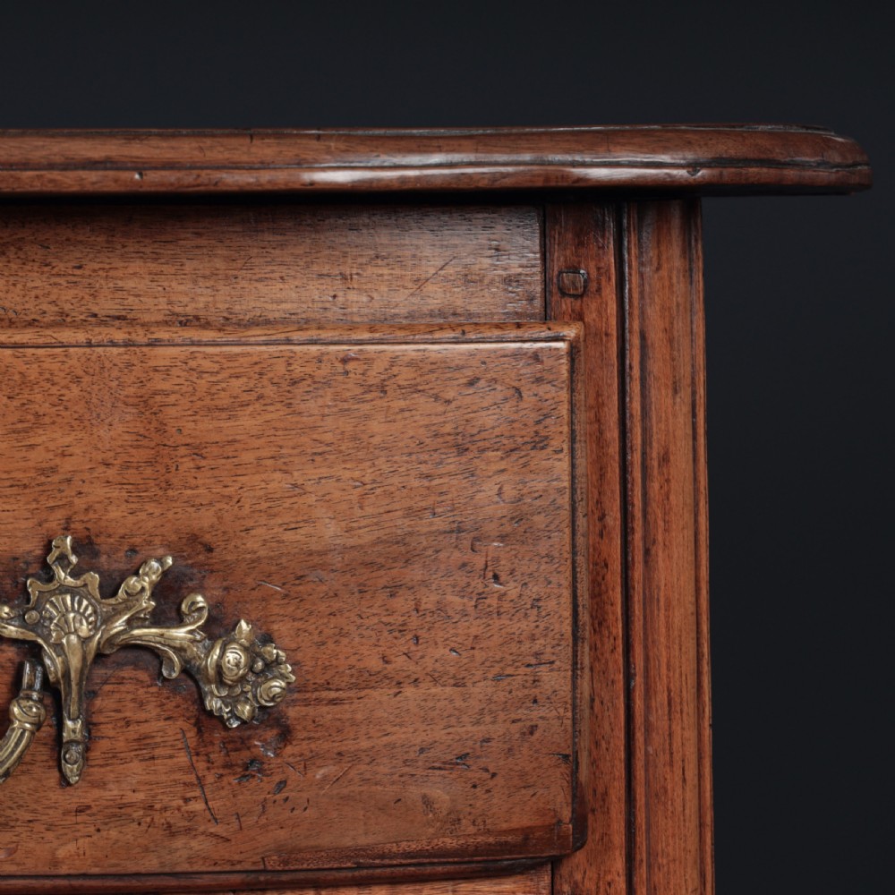 A French Louis XV style warm walnut commode featuring four drawer levels with ornate brass scroll handles and keyhole escutcheons. View II