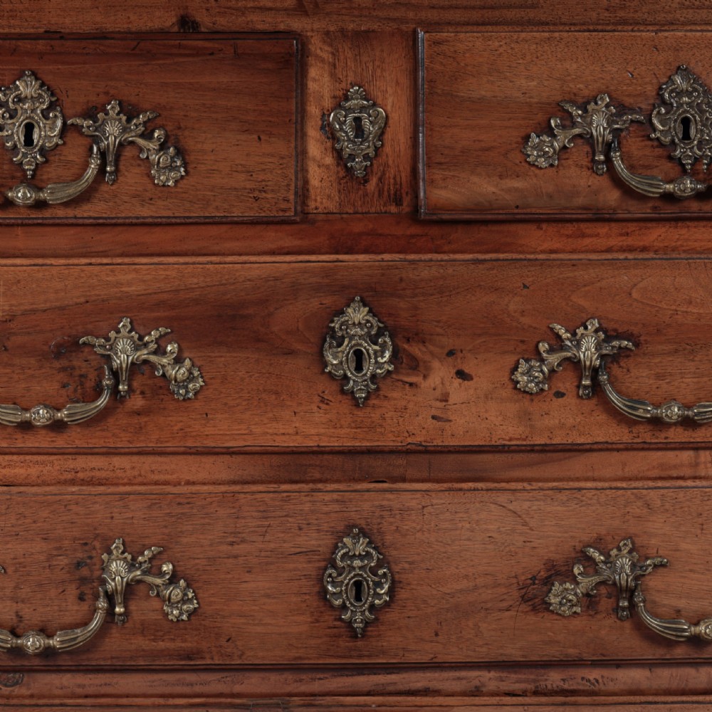 A French Louis XV style warm walnut commode featuring four drawer levels with ornate brass scroll handles and keyhole escutcheons. View III