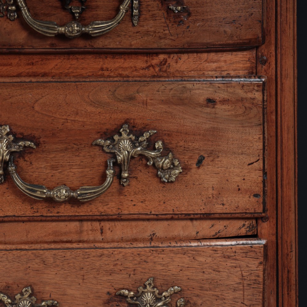 A French Louis XV style warm walnut commode featuring four drawer levels with ornate brass scroll handles and keyhole escutcheons. View V