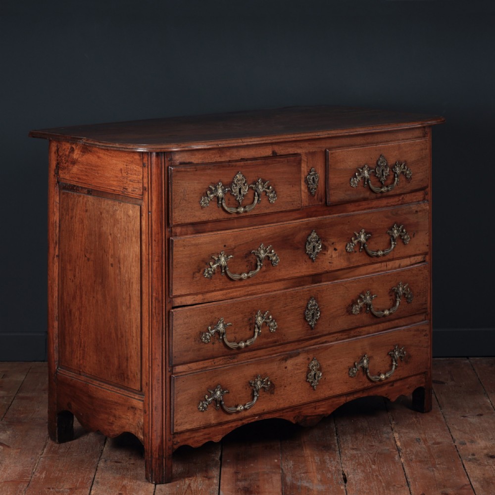 A French Louis XV style warm walnut commode featuring four drawer levels with ornate brass scroll handles and keyhole escutcheons. View VII