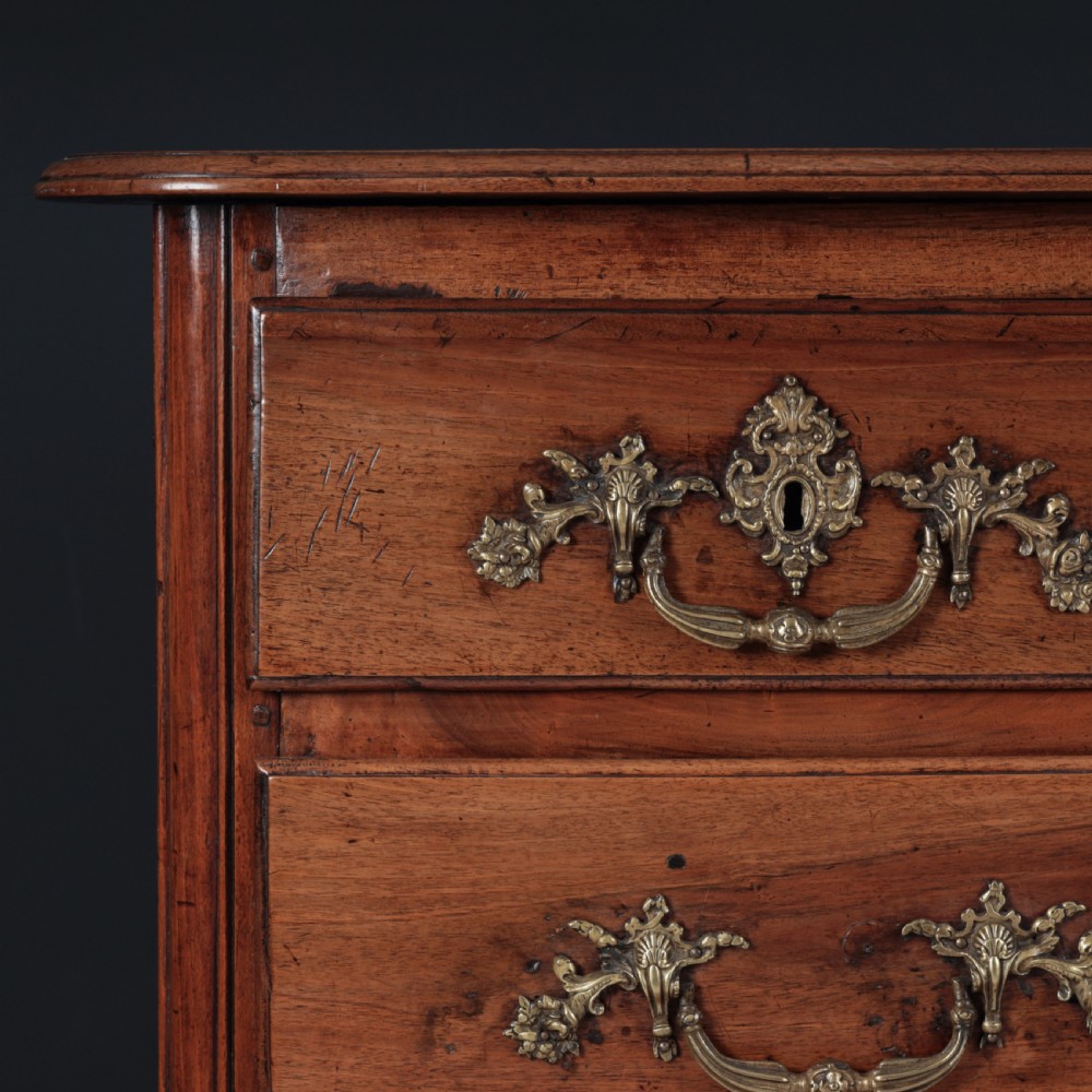 A French Louis XV style warm walnut commode featuring four drawer levels with ornate brass scroll handles and keyhole escutcheons. View VIII