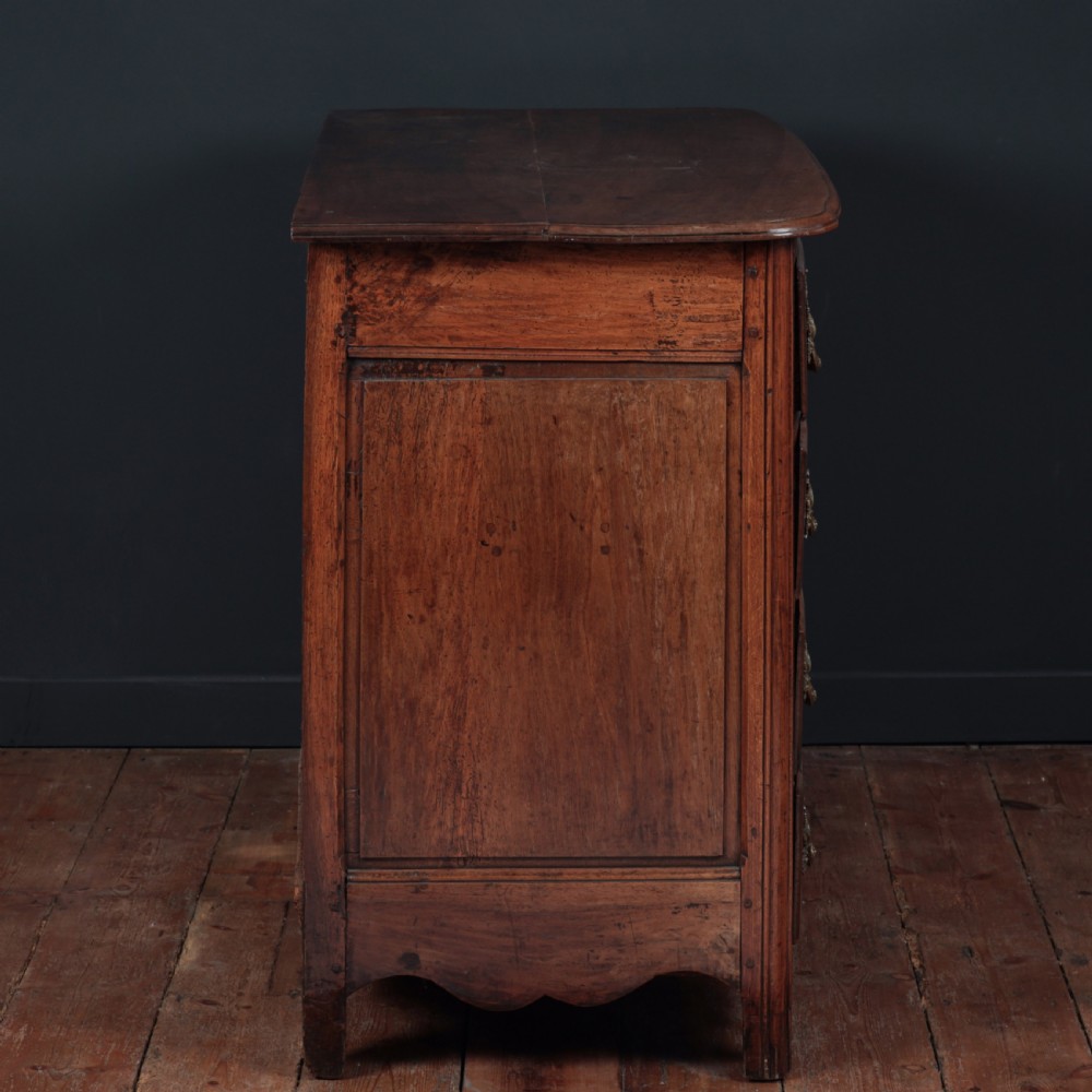 A French Louis XV style warm walnut commode featuring four drawer levels with ornate brass scroll handles and keyhole escutcheons. View IX
