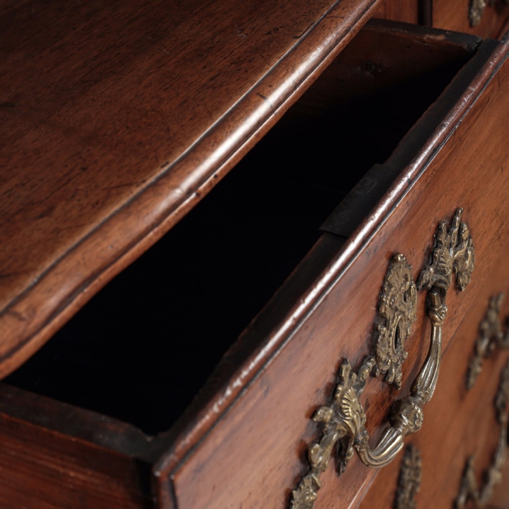 A French Louis XV style warm walnut commode featuring four drawer levels with ornate brass scroll handles and keyhole escutcheons. View XII