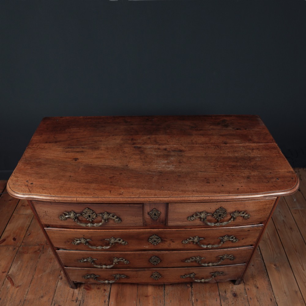 A French Louis XV style warm walnut commode featuring four drawer levels with ornate brass scroll handles and keyhole escutcheons. View XIV