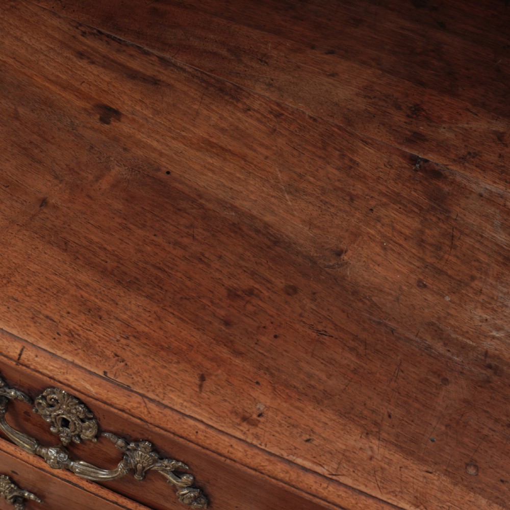 A French Louis XV style warm walnut commode featuring four drawer levels with ornate brass scroll handles and keyhole escutcheons. View XVI