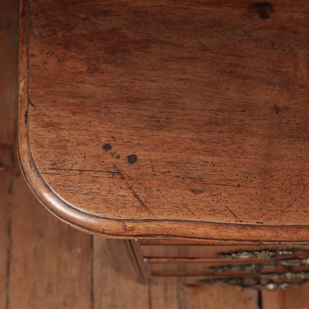 A French Louis XV style warm walnut commode featuring four drawer levels with ornate brass scroll handles and keyhole escutcheons. View XVII