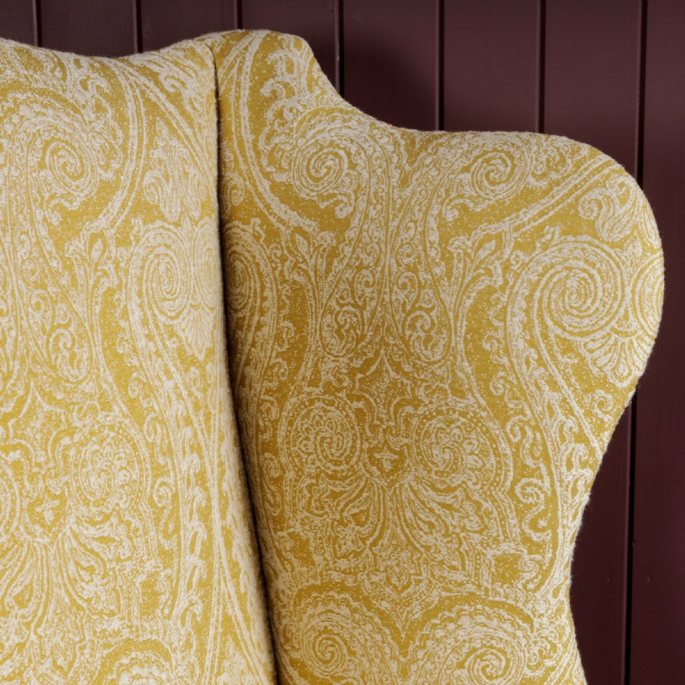 A high-backed Regency wingback armchair upholstered in patterned yellow fabric with turned mahogany front legs on brass castors. View II